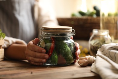 Woman holding glass jar of pickled cucumbers at wooden table, closeup