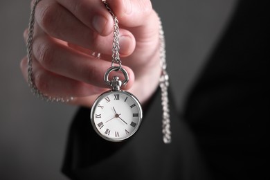 Man holding chain with elegant pocket watch on blurred background, closeup