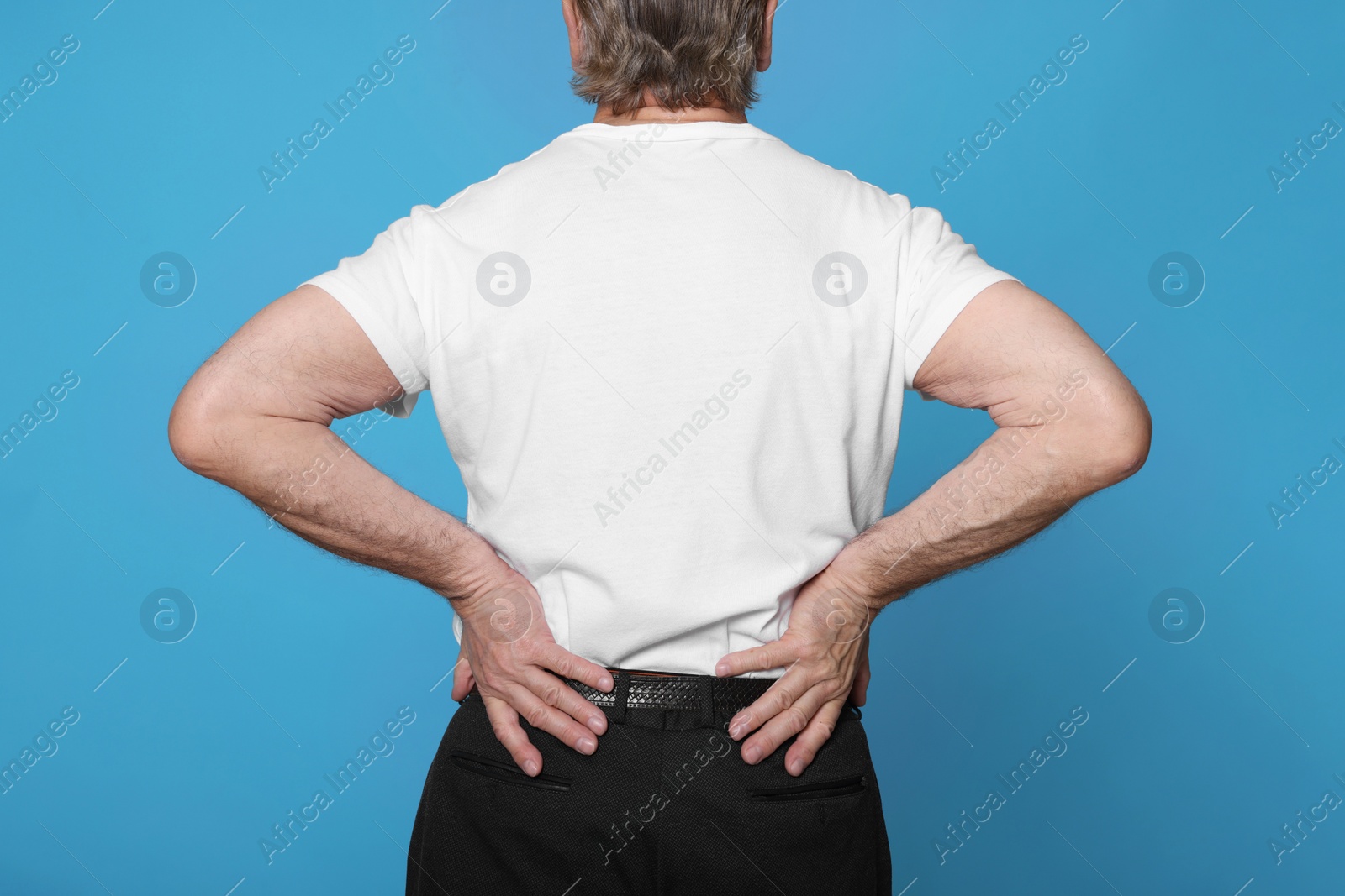 Photo of Senior man suffering from pain in back on light blue background. Arthritis symptoms