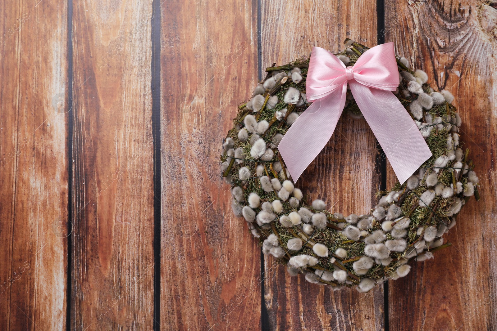 Photo of Wreath made of beautiful willow branches and pink bow on wooden background, top view. Space for text