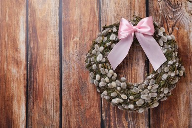 Photo of Wreath made of beautiful willow branches and pink bow on wooden background, top view. Space for text