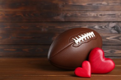 American football ball and hearts on wooden table. Space for text