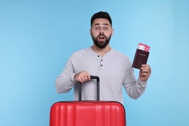 Photo of Surprised man with passport, tickets and suitcase on light blue background