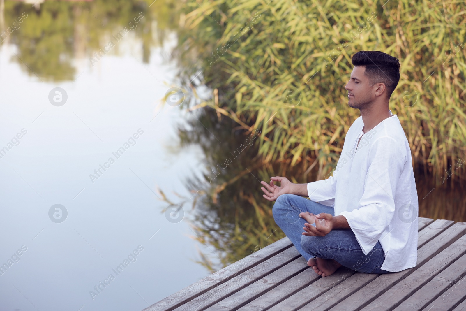 Photo of Man meditating on wooden pier near river. Space for text