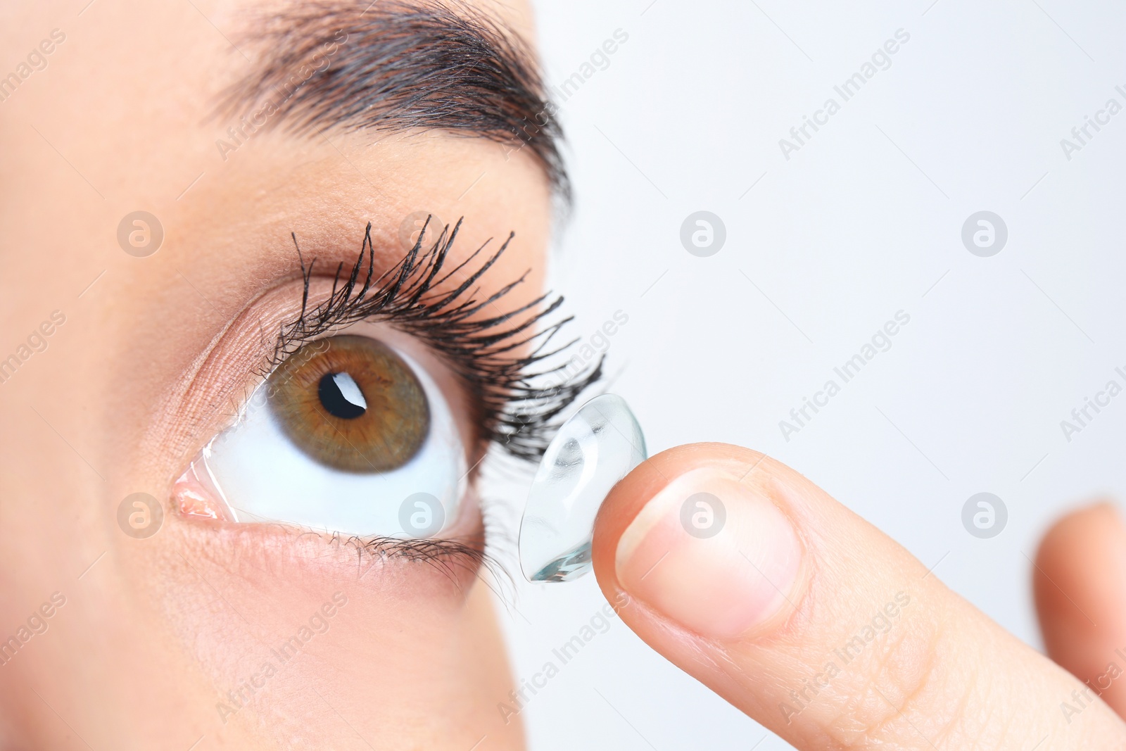 Photo of Young woman putting contact lens in her eye, closeup