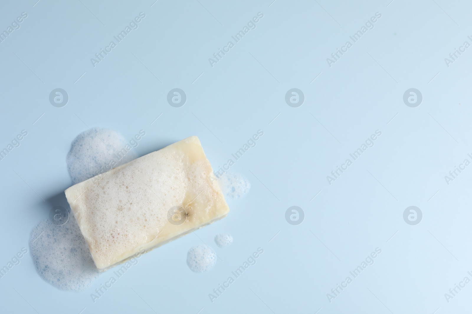 Photo of Soap with fluffy foam on light blue background, top view. Space for text