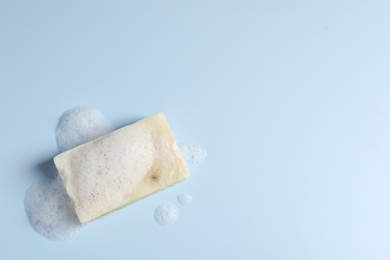 Photo of Soap with fluffy foam on light blue background, top view. Space for text