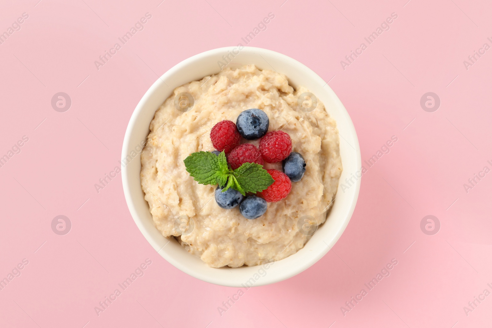 Photo of Tasty oatmeal porridge with raspberries and blueberries in bowl on pink background, top view