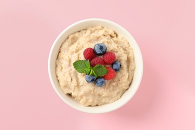 Photo of Tasty oatmeal porridge with raspberries and blueberries in bowl on pink background, top view