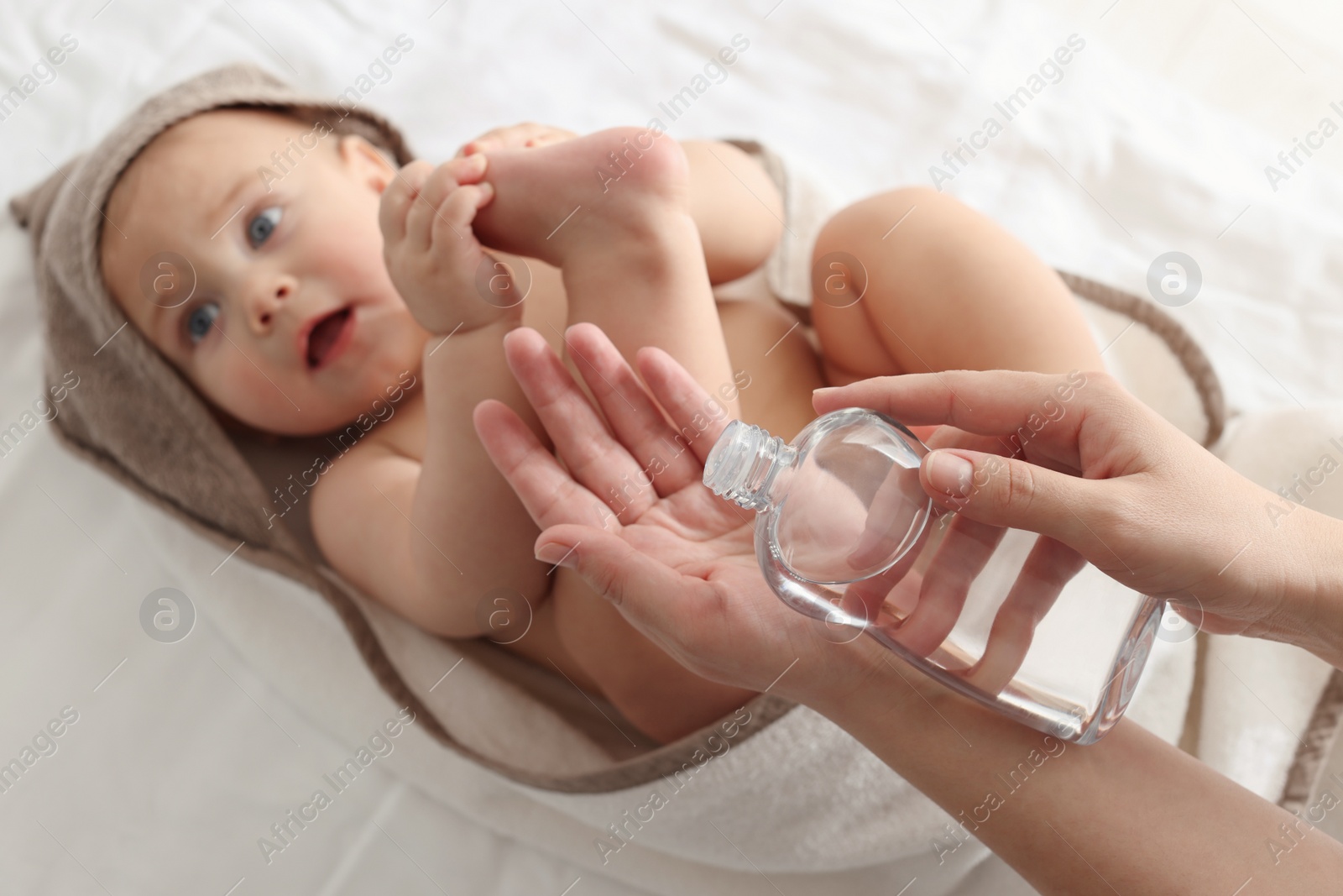 Photo of Mother with bottle of massage oil near baby on bed, closeup