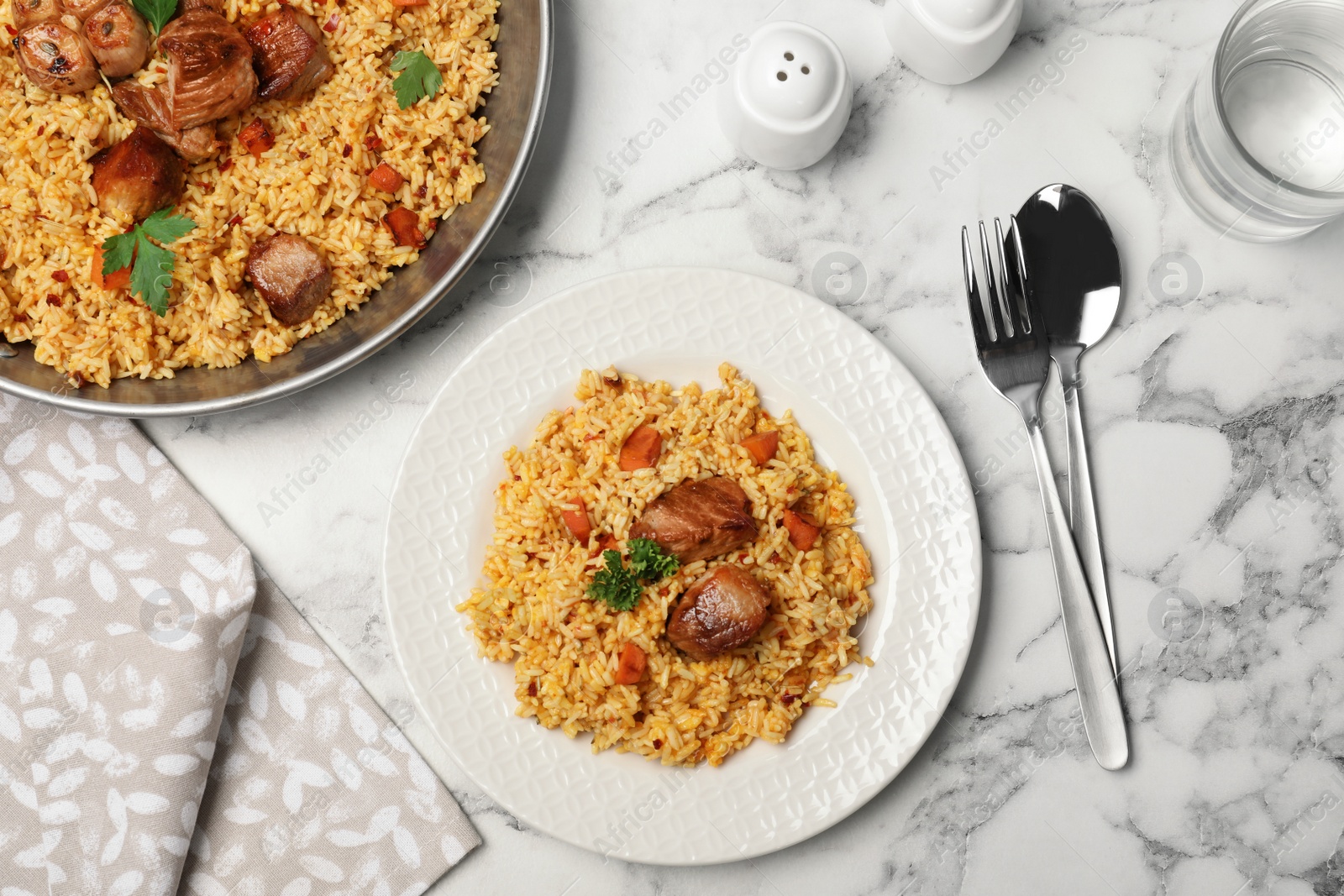 Photo of Tasty rice pilaf with meat served on marble table, flat lay