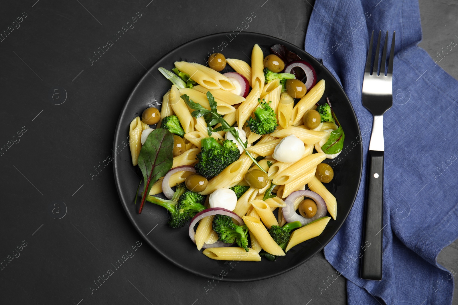 Photo of Plate of delicious pasta with broccoli, onion and olives on black table, flat lay