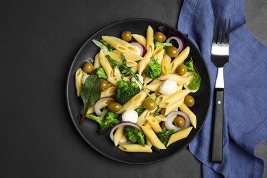 Photo of Plate of delicious pasta with broccoli, onion and olives on black table, flat lay