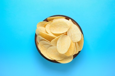 Photo of Bowl with delicious potato chips on light blue background, top view