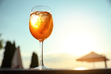 Photo of Glass of fresh summer cocktail on table outdoors at sunset, low angle view. Space for text