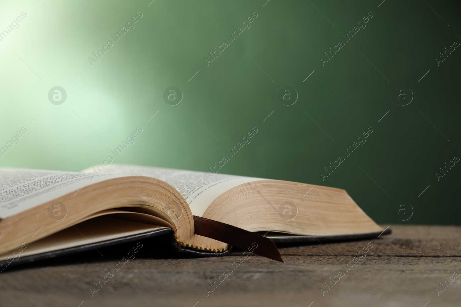 Photo of Open Bible on wooden table against green background. Space for text