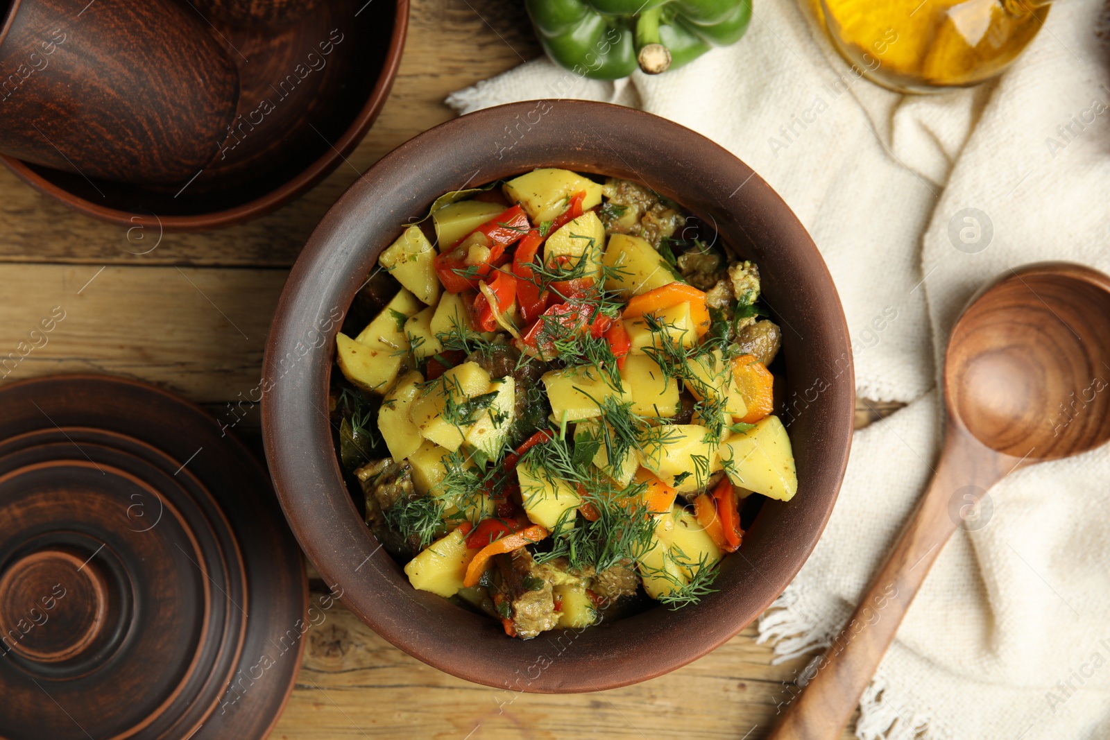 Photo of Tasty cooked dish with potatoes in earthenware served on wooden table, flat lay