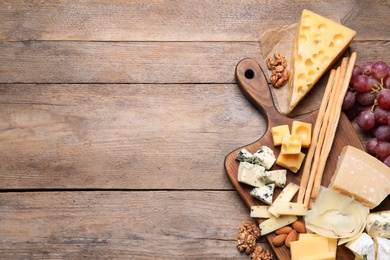 Photo of Cheese plate with grapes and nuts on wooden table, top view. Space for text