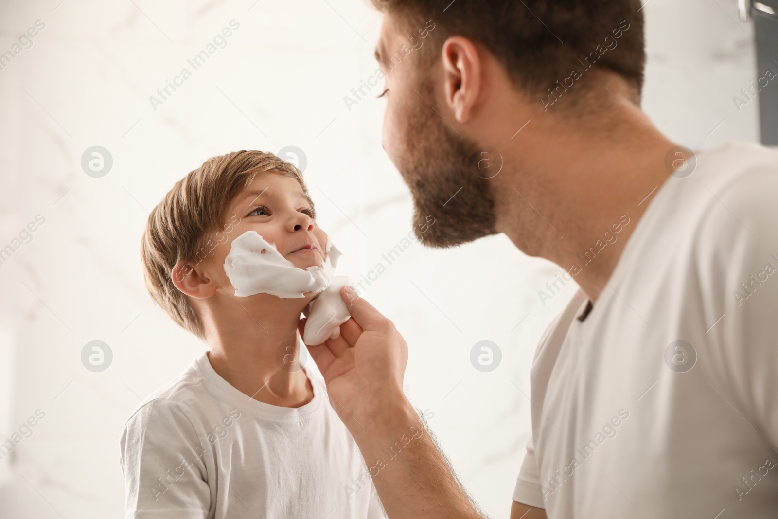 Photo of Dad applying shaving foam onto son's face in bathroom