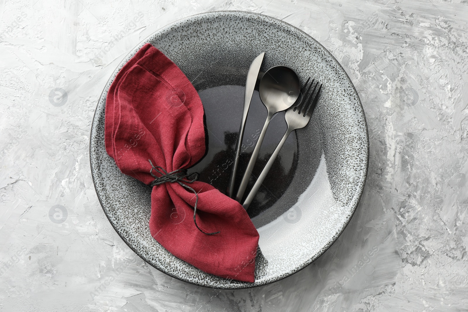 Photo of Stylish setting with cutlery, napkin and plate on grey textured table, top view