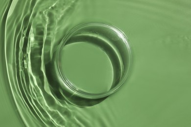 Photo of Stylish presentation for product. Glass podium in water on pale green background, top view