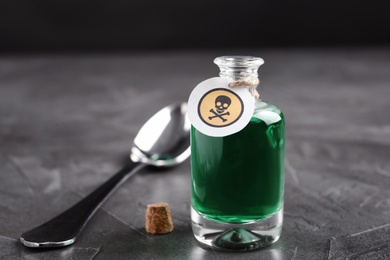 Photo of Glass bottle of poison with warning sign and spoon on grey stone table