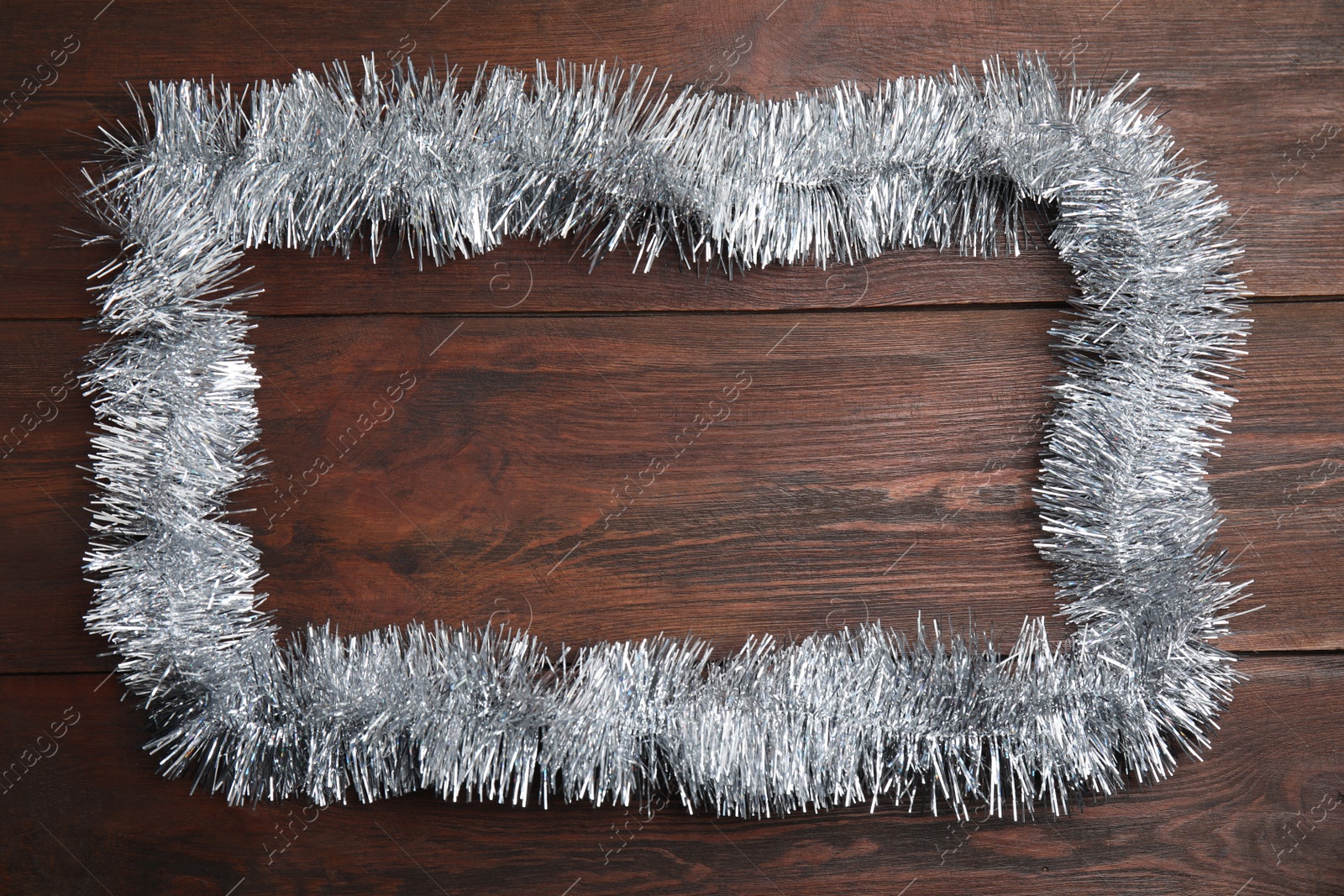 Photo of Frame of silver tinsel on wooden background, top view. Space for text