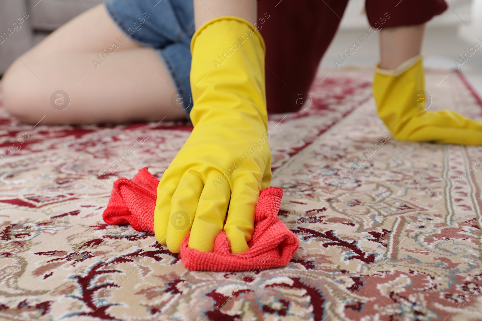 Photo of Woman in rubber gloves cleaning carpet with rag indoors, closeup