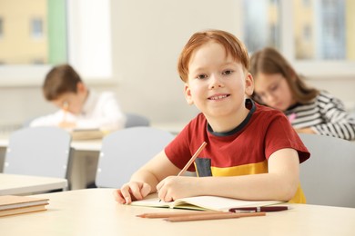 Portrait of smiling little boy studying in classroom at school. Space for text