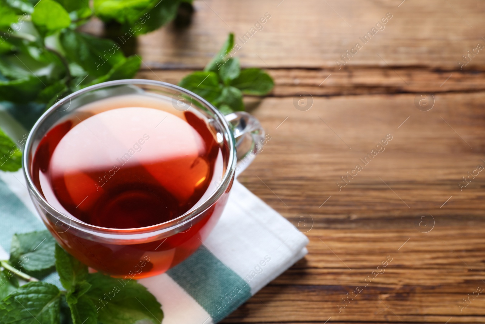 Photo of Cup with hot aromatic mint tea on wooden table, closeup. Space for text