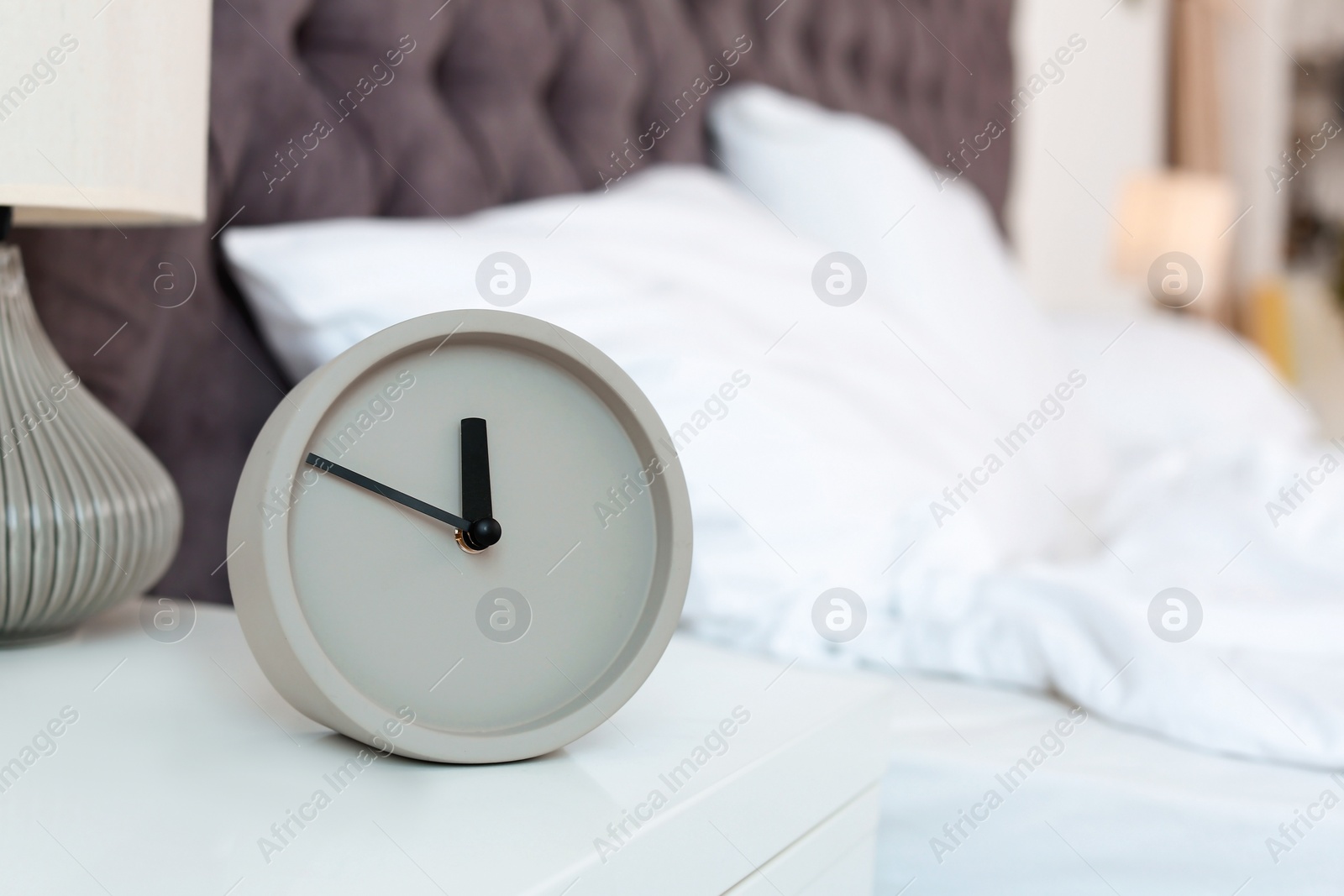 Photo of Analog alarm clock on table in bedroom. Time of day