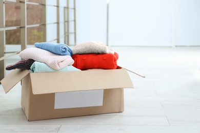 Donation box with clothes on floor indoors. Space for text