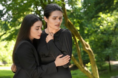 Photo of Sad women in black clothes mourning outdoors, space for text. Funeral ceremony