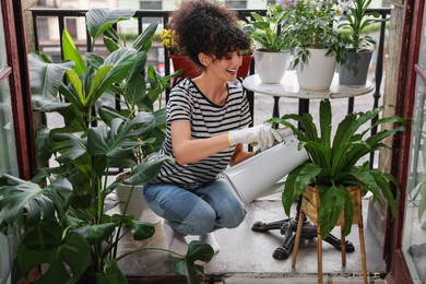 Happy young woman watering green potted houseplants on balcony