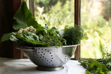 Photo of Different herbs in colander near window indoors