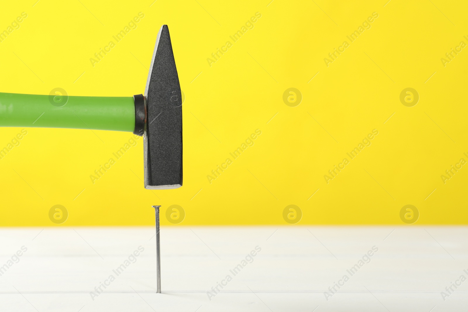 Photo of Hammering metal nail on white wooden table against yellow background. Space for text