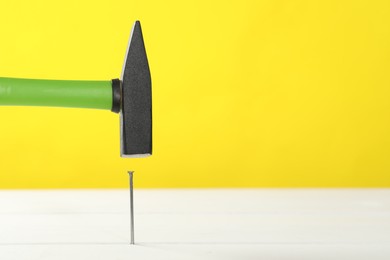 Hammering metal nail on white wooden table against yellow background. Space for text