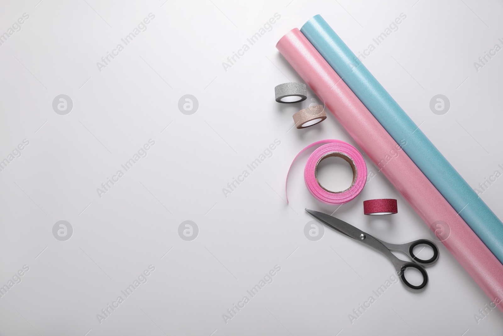 Photo of Rolls of colorful wrapping papers, scissors and ribbons on white background, flat lay. Space for text