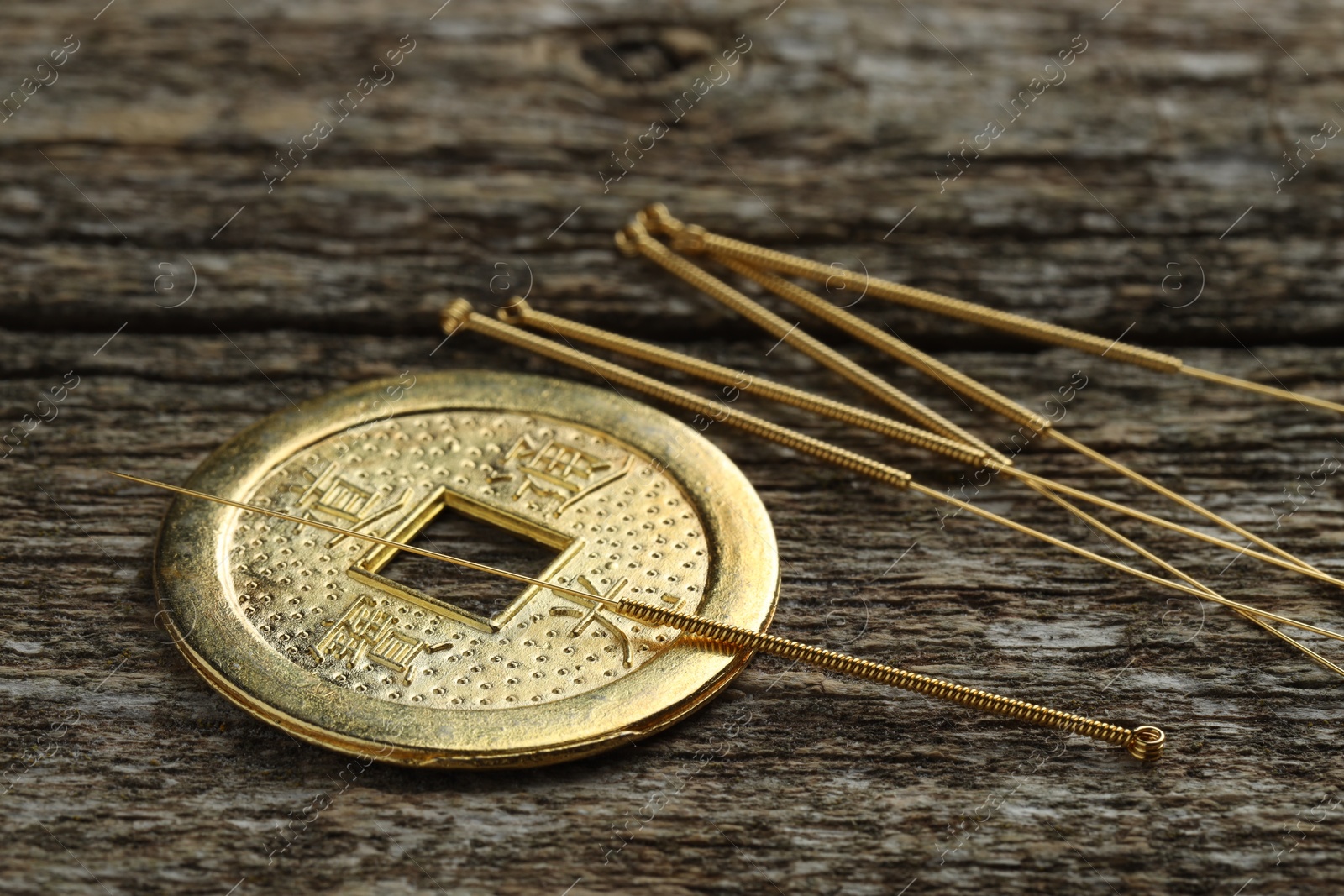 Photo of Acupuncture needles and Chinese coin on wooden table, closeup