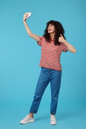 Beautiful young woman taking selfie on light blue background