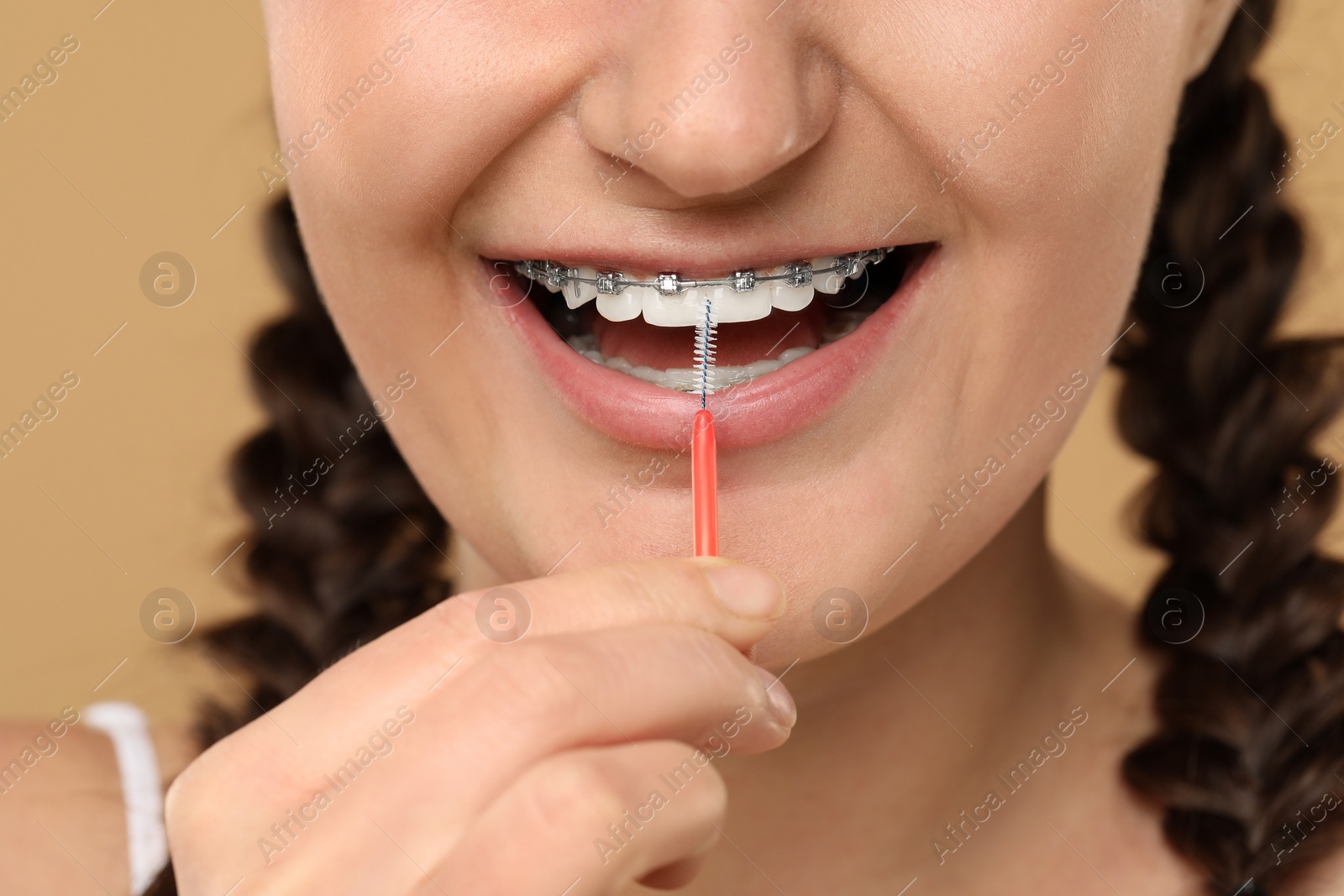 Photo of Woman with dental braces cleaning teeth using interdental brush on brown background, closeup