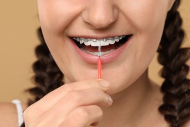 Photo of Woman with dental braces cleaning teeth using interdental brush on brown background, closeup