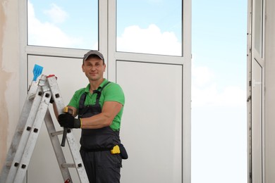 Photo of Worker standing on folding ladder indoors. Window installation