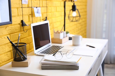 Stylish home office interior with comfortable workplace near yellow brick wall