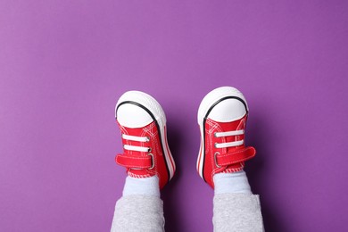 Photo of Little child in stylish red gumshoes on purple background, top view