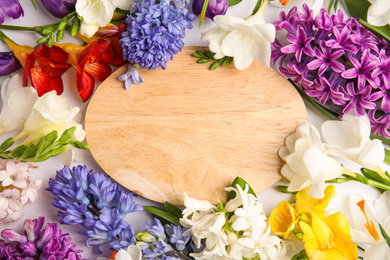 Beautiful spring flowers and wooden board on white background, flat lay. Space for text