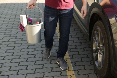 Photo of Man holding bucket with car cleaning products outdoors, closeup