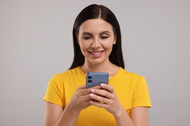 Young woman using smartphone on grey background