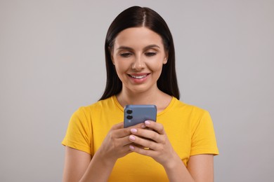 Photo of Young woman using smartphone on grey background