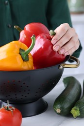 Woman holding black colander with bell pepper at white table, closeup